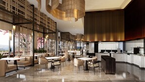 Um saguão de hotel moderno, com disposição espaçosa, área de estar central e uma cozinha visível ao fundo.