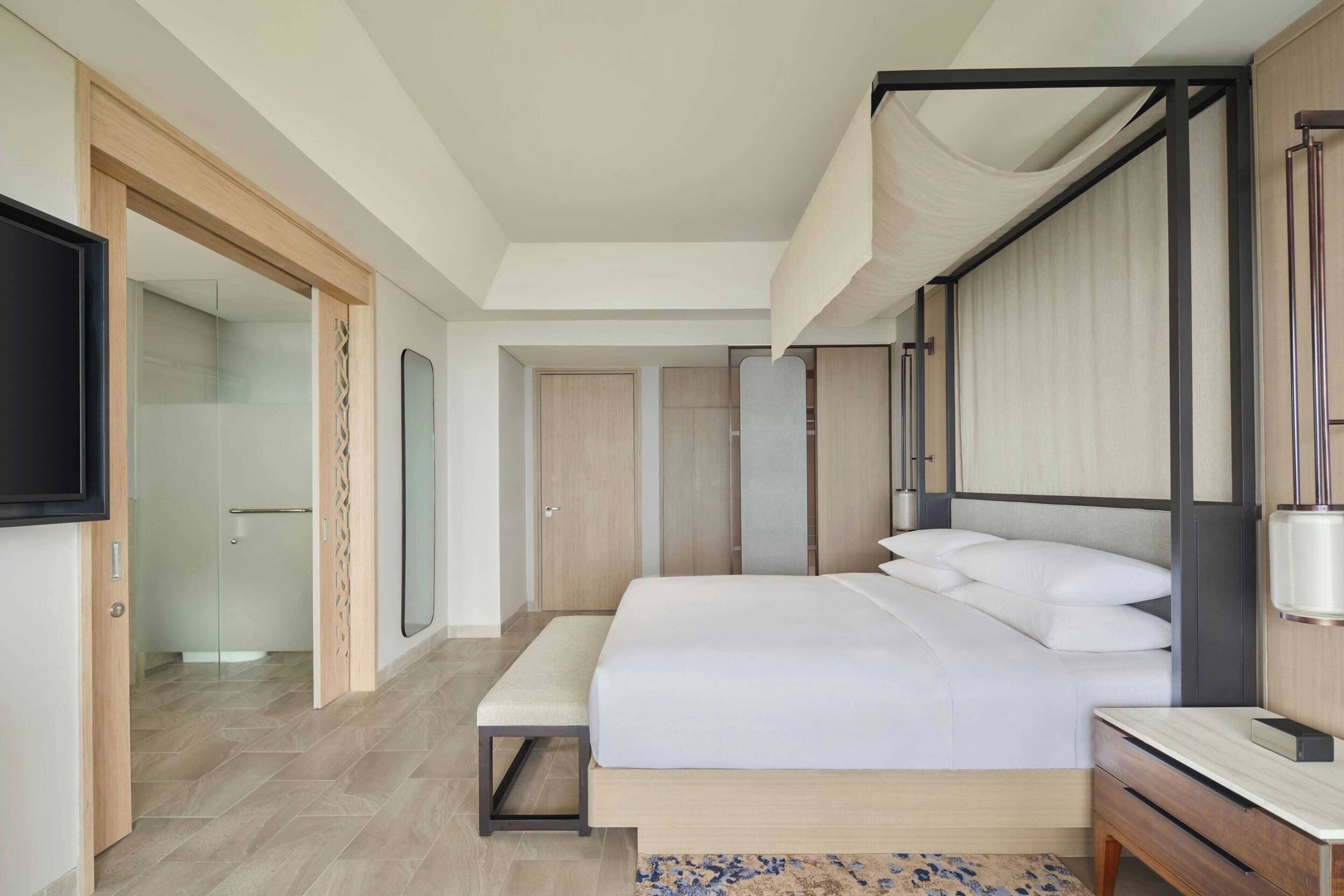 A modern hotel room with a large bed, bedside tables, a flat-screen TV, and a walk-in closet.