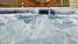 A hot tub with a wooden hammock, stone walls, and a mountain view. - Walser cabin with rock SPA and Monte Rosa views (Alagna Valsesia)