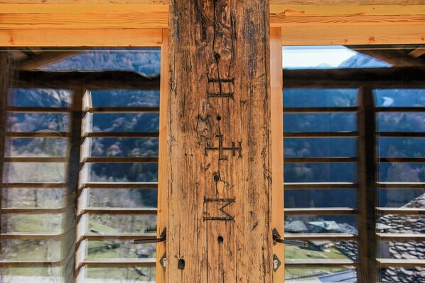 A wooden beam with carved letters, a window with a view of mountains, and a wooden structure. - Walser cabin with rock SPA and Monte Rosa views (Alagna Valsesia)