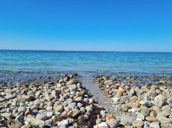 Ein felsiger Strand mit klarem Wasser und blauem Himmel.
