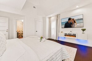Quarto com cama, televisão, lareira e banheiro visível através de uma porta aberta.