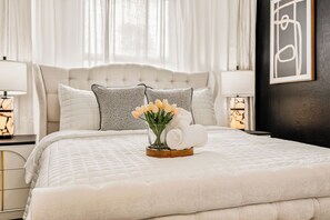 Ein ordentlich bezogenes Bett mit weißer Decke, eine Vase mit Blumen und zusammengerollte Handtücher auf einem Holztablett.