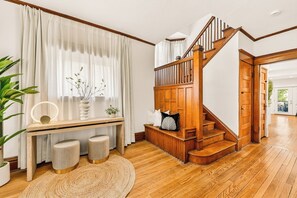 Uma escada com guarda-corpos de madeira, uma mesa consola com um vaso e um espelho, e um tapete redondo sobre piso de madeira.