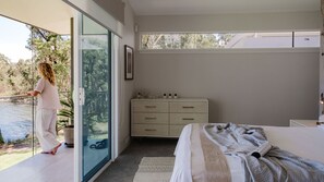 Ein Schlafzimmer mit Bett, Kommode, Fenster und Blick auf ein Gewässer.