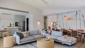 Ein modernes Wohnzimmer mit einem grauen Ecksofa, einem runden Couchtisch und einem Essbereich mit Holzsesseln und einem Tisch.