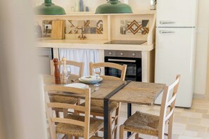 Ein Essbereich mit Holztisch und -stühlen, eine Küche mit Herd und Backofen sowie ein weißer Kühlschrank.