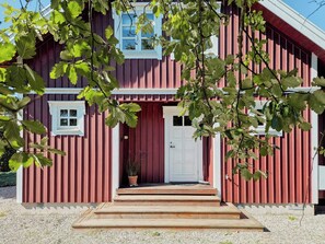 Ein rotes, auf einen Bauernhof abgestimmtes Gebäude mit einer weißen Tür, einem kleinen Fenster und einem Blumentopf auf der Veranda.