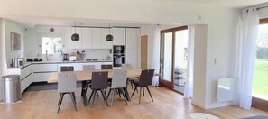 A modern kitchen with white cabinets, a wooden dining table, and a large window. - Villa with panoramic views of the French Riviera (La Gaude)