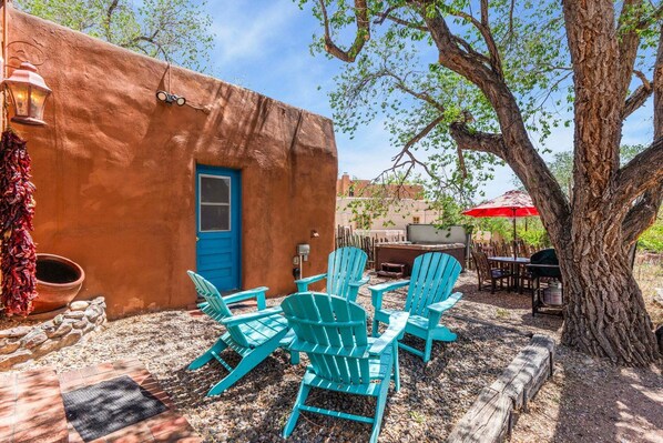 Un patio con sillas Adirondack turquesas, una puerta azul y un paraguas rojo.