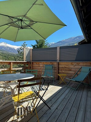 A wooden deck with a round table and chairs, a green umbrella, and a view of snow-capped mountains. - Renovated little house with High Alps view (Baratier)