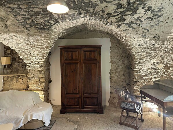 A room with a stone wall, a wooden wardrobe, a white sofa, and a rocking chair. - Renovated little house with High Alps view (Baratier)