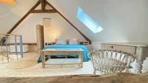 A bedroom with a sloped ceiling, a bed with blue bedding, a white chair, a small table, and a hanging light fixture. - Renovated little house with High Alps view (Baratier)