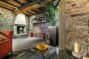 Ein Zimmer mit Stehwänden, einem Kamin, einer Couch, einem Glastisch und einer Topfpflanze.