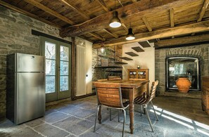 Eine rustikale Küche mit Steinwänden, einer Holzbalkendecke, einem eingebauten Kühlschrank, einem Holzespeisetisch mit Stühlen und einem Steinfußboden.