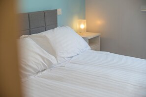 Ein Bett mit weißer Bettwäsche, ein grauer Kopfteil und ein Nachttisch mit Lampe.