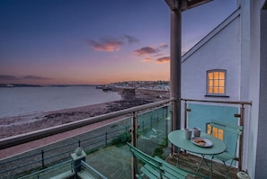 Ein Balkon mit Tisch und Stühlen mit Blick auf einen Strand und eine entfernte Stadt.