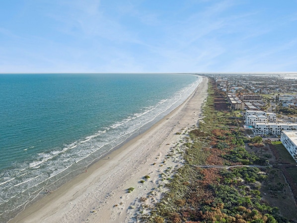 Luftaufnahme einer Küstenstadt mit Strand, Gebäuden und Grünflächen.