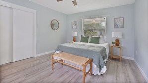 Ein Schlafzimmer mit einem Bett, Nachttischen, einem Deckenventilator, einer Bank und einem Fenster mit Jalousien.