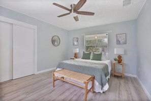 Ein Schlafzimmer mit einem Bett, Nachttischen, einem Deckenventilator, einer Bank und einem Fenster mit Jalousien.