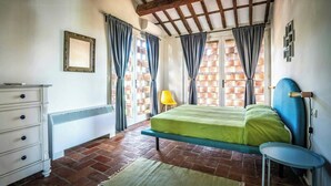 A bedroom with a bed, a dresser, a chair, and a window with curtains. - Charming apartment on a vineyard near Lucca (Segromigno in Monte)