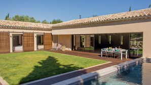A backyard with a swimming pool, a patio with a table and chairs, and a covered area with a table and chairs.