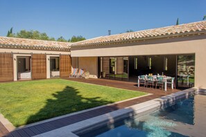 Ein Garten mit Swimmingpool, einer Terrasse mit Tisch und Stühlen und einem überdachten Bereich mit Tisch und Stühlen.