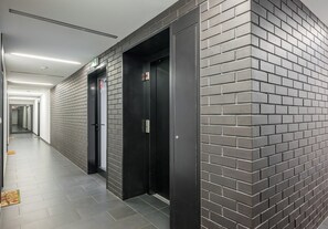 A hallway with two elevators, a tiled floor, and a brick wall. - Fabryka na Pradze Charming Apartment (Warszawa)