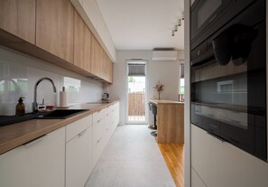 A modern kitchen with a wooden countertop, stainless steel appliances, and a view to the outside. - Fabryka na Pradze Charming Apartment (Warszawa)
