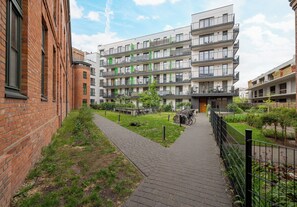 A multi-story residential building with a brick facade, a paved walkway, and a small garden area. - Fabryka na Pradze Charming Apartment (Warszawa)
