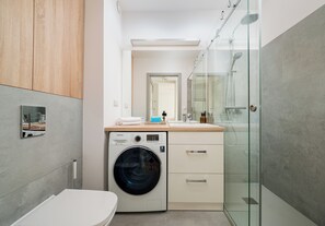 Ein kleines Badezimmer mit Waschmaschine, Duschkabine und Waschbecken mit Spiegel.