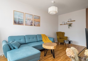 Una sala moderna con un sofá seccional, una mesa de centro redonda de madera, un sillón amarillo, una lámpara colgante blanca y obras de arte en la pared.