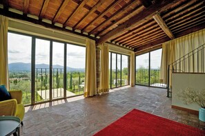 Ein geräumiges Zimmer mit großen Fenstern, einem roten Teppich und Blick ins Grüne.