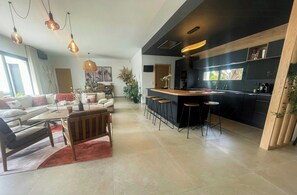 A modern kitchen with a bar area, a dining area with a sofa and chairs, and a living room with a coffee table and a fireplace. - Designer villa near the Gulf of Saint-Tropez (Grimaud)