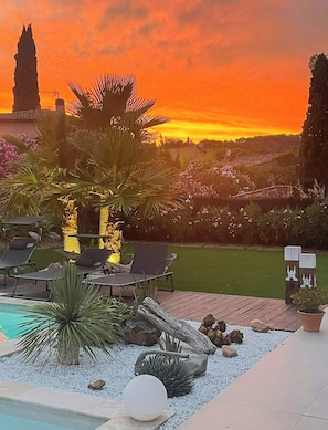 A poolside area with lounge chairs, a small waterfall feature, and a view of a sunset. - Designer villa near the Gulf of Saint-Tropez (Grimaud)