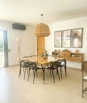 A dining area with a round table, six chairs, a hanging light fixture, and wall-mounted artwork. - Designer villa near the Gulf of Saint-Tropez (Grimaud)