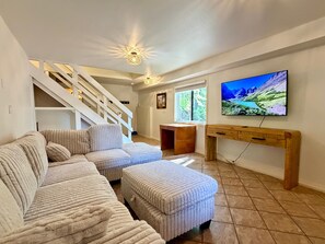 A living room with a sectional sofa, a wooden console table, a TV mounted on the wall, and a staircase. - Experience Whitefish Retreat at Poplar Place, a 3-bedroom haven in scenic Whitefish, MT. (Whitefish)