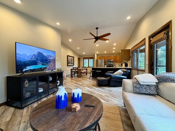 A modern living room with a flat-screen TV, a ceiling fan, a dining area, and a kitchen. - Experience Whitefish Retreat at Poplar Place, a 3-bedroom haven in scenic Whitefish, MT. (Whitefish)