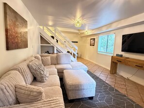 Un salon moderne avec un canapé d’angle, un escalier, un téléviseur à écran plat et un tapis à motifs.