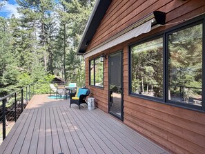 A wooden deck with outdoor furniture, large windows, and a view of a forest. - Experience Whitefish Retreat at Poplar Place, a 3-bedroom haven in scenic Whitefish, MT. (Whitefish)