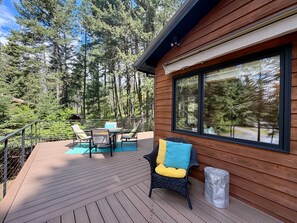 A wooden deck with outdoor furniture, a large window, and a forest backdrop. - Experience Whitefish Retreat at Poplar Place, a 3-bedroom haven in scenic Whitefish, MT. (Whitefish)