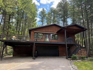 A two-story cabin with a garage, surrounded by tall trees. - Experience Whitefish Retreat at Poplar Place, a 3-bedroom haven in scenic Whitefish, MT. (Whitefish)