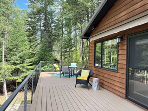 Una terraza de madera con muebles de exterior, rodeada de un bosque.