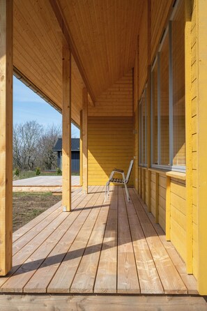Eine Holzterrasse mit überdachtem Bereich, einem Stuhl und einem Fenster.