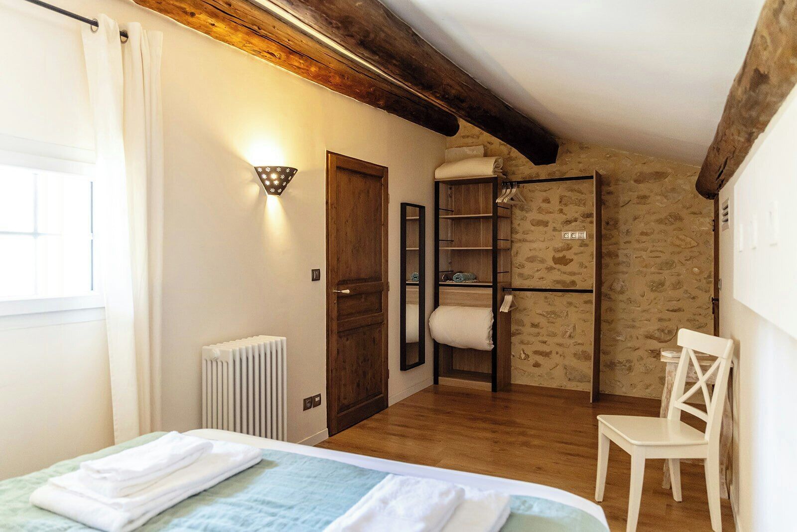 Una camera da letto con un letto, una sedia, un termosifone, una porta in legno e un muro in pietra.