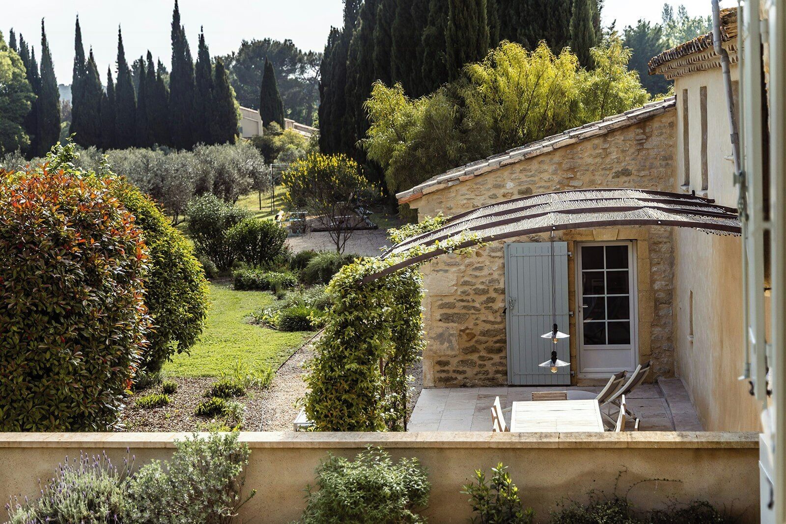 Un bâtiment en pierre doté d’un patio couvert, d’un jardin agrémenté de divers arbustes et arbres, et offrant une vue sur le paysage environnant.