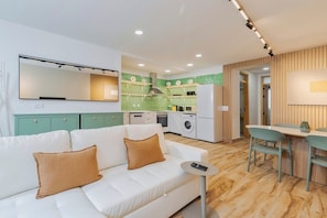 A modern living room with a white sofa, a small round table, and a kitchen area with green tiles and white appliances. - Setúbal Heritage House (Setúbal)
