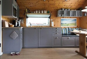 A kitchen with grey cabinets, a wooden ceiling, a window with a view, and a dining area with a table and bench. - Sleep under the stars near Brunsnæs Beach (Broager)