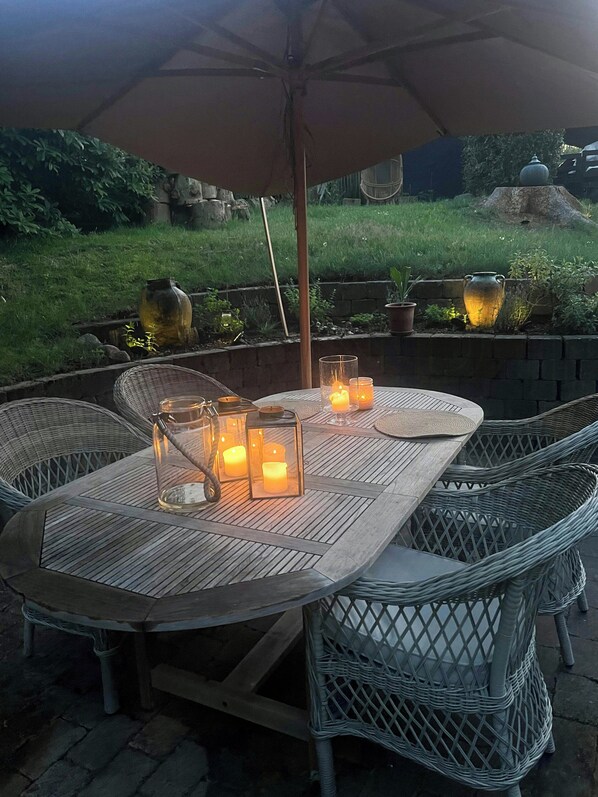 Eine Terrasse im Freien mit einem runden Tisch, Korbstühlen und einem großen Sonnenschirm.