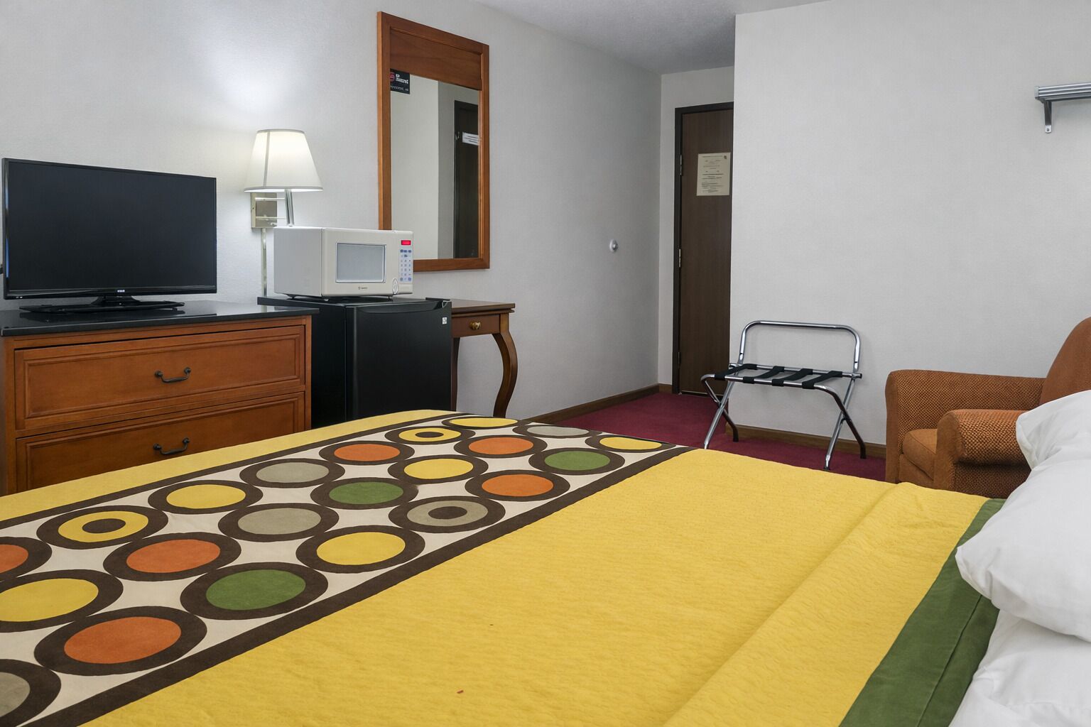 A hotel room with a bed, a television, a microwave, a dresser, a chair, and a mirror.